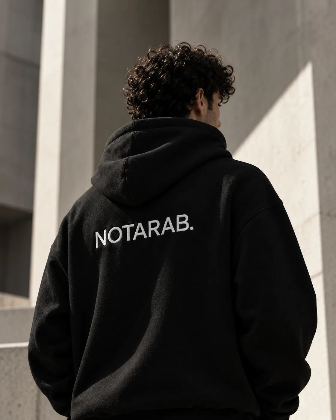 Back of a NOTARAB. hoodie against a concrete wall